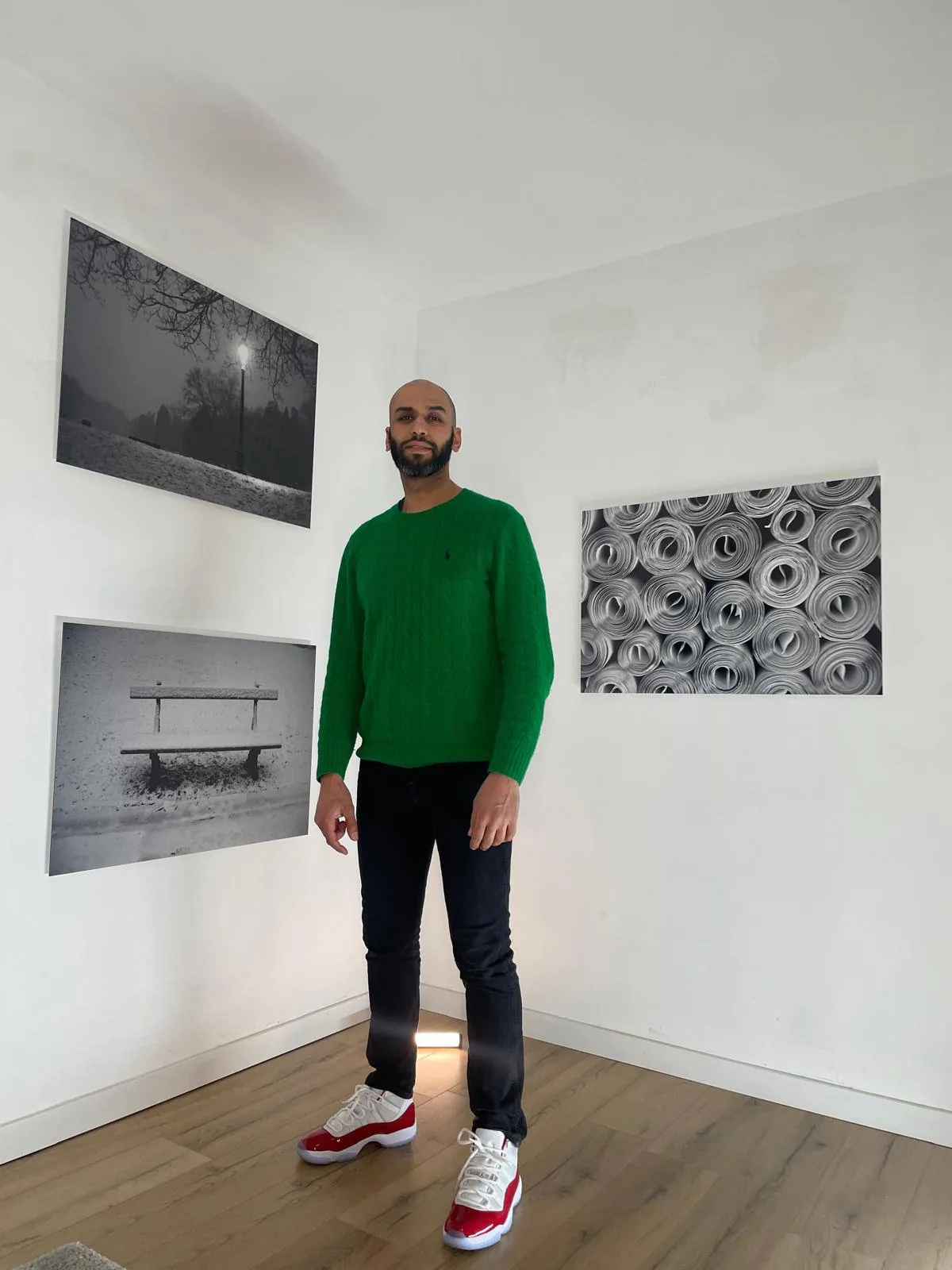 Mejdoub El Ghiwane debout entre ses tirages noir et blanc accrochés au mur